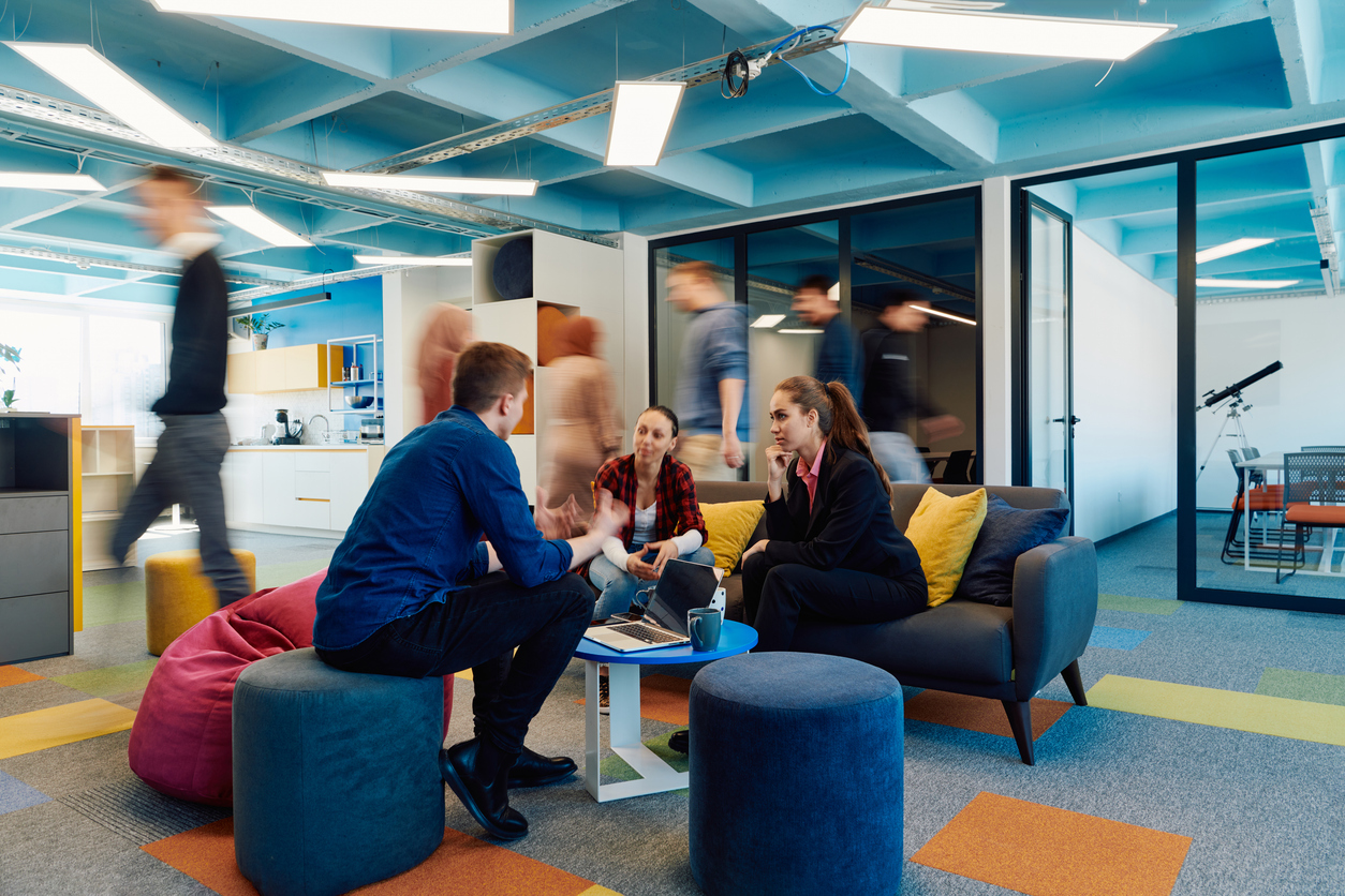 Multiethnic startup business team on meeting in a modern bright open space coworking office. Brainstorming, working on laptop. Group of coworkers walking around in motion blur coworking spaces